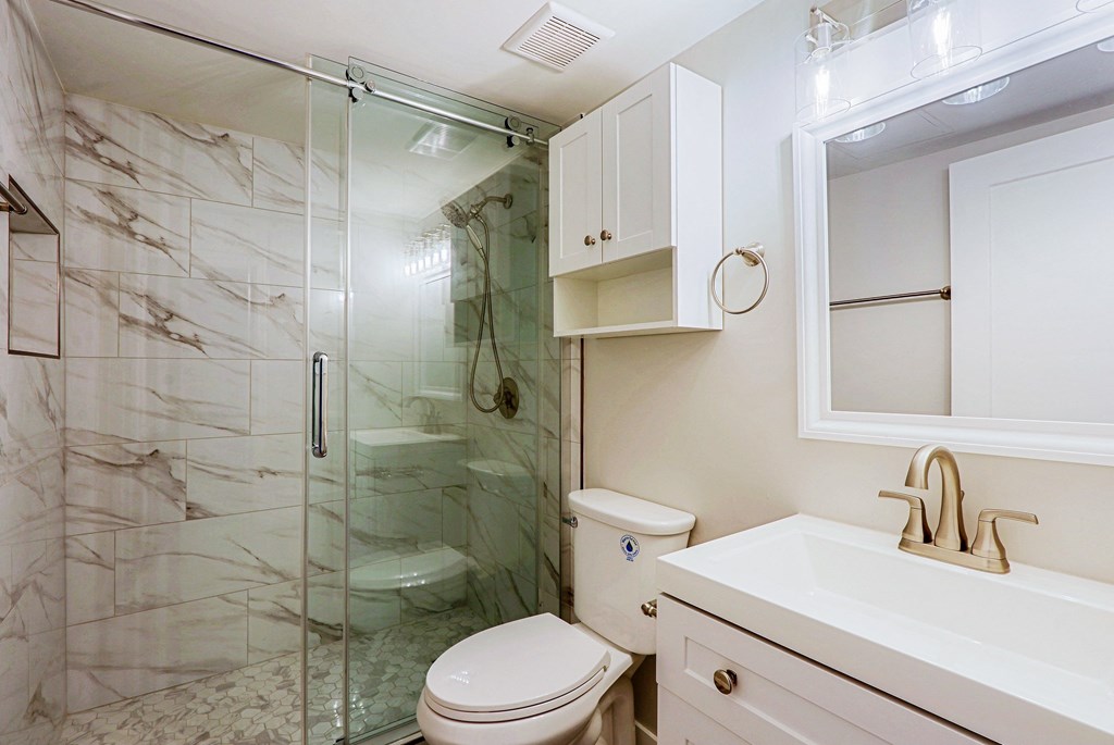 A white toilet sits in a bathroom with a marble wall and a glass shower.