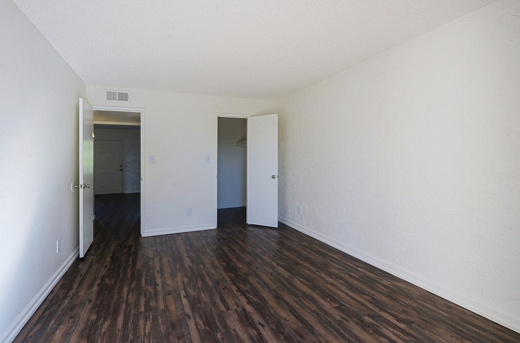 A room with white walls and wood flooring with two doors.