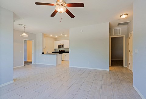 an empty living room with a ceiling fan and a kitchen