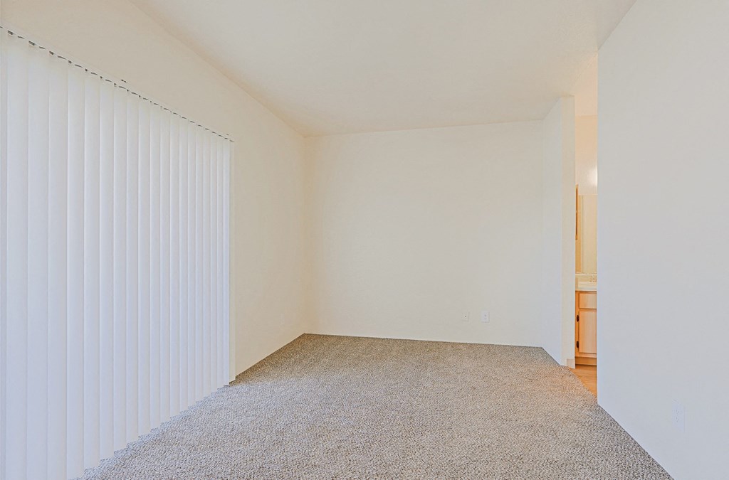 a spacious living room with white walls and a window with white blinds