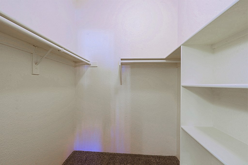 a walk in closet with white walls and shelves and two white shelves on the wall