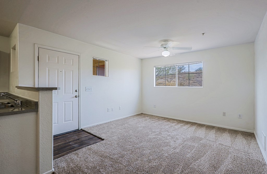 A room with a carpeted floor, a ceiling fan, and a window showing a view of a field.