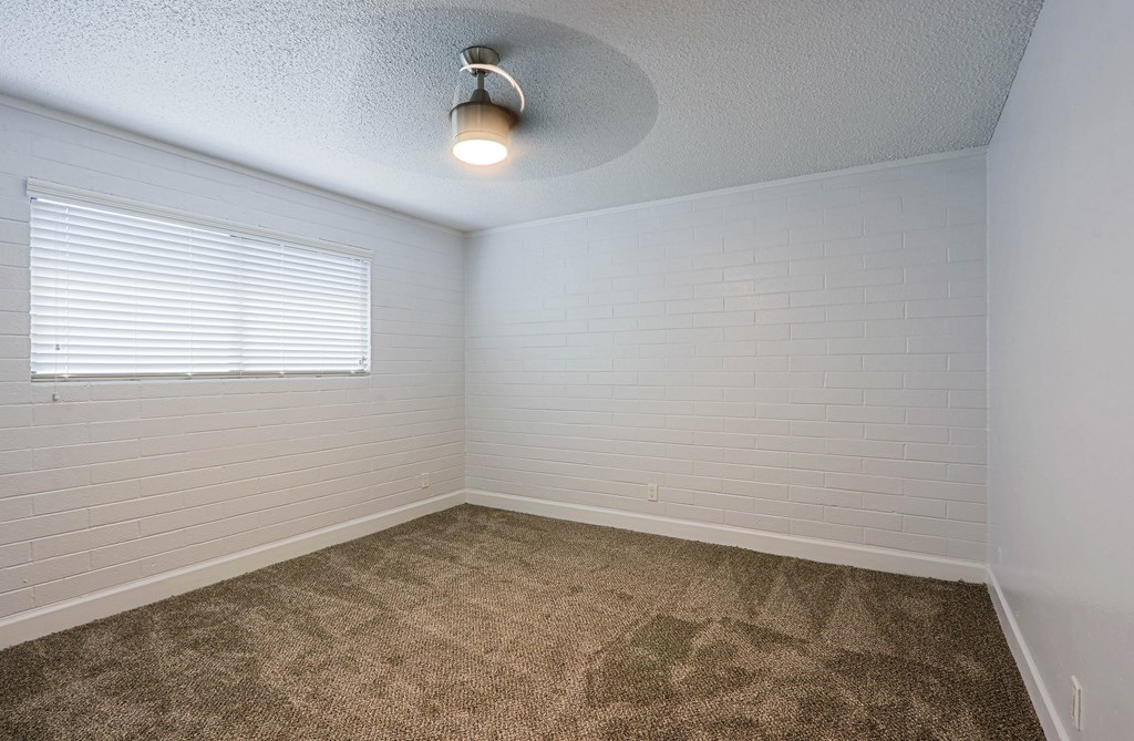 A room with a carpeted floor and a window with blinds.