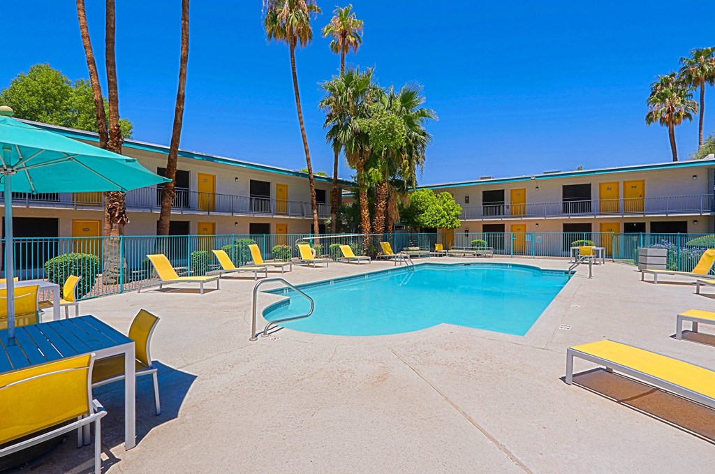 A pool area with yellow and blue lounge chairs and a blue umbrella.