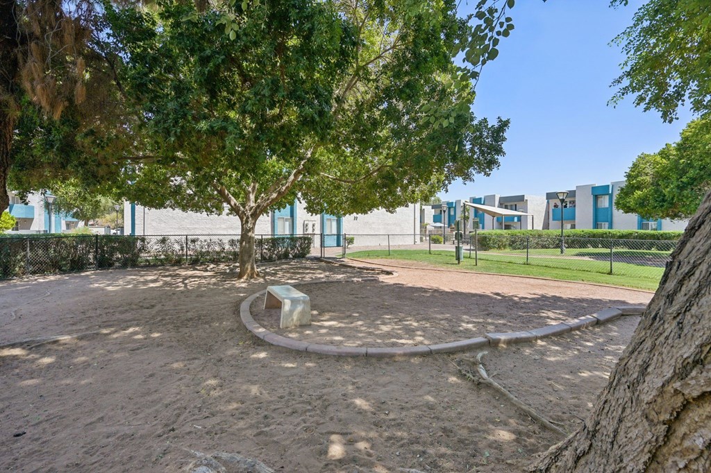 A playground with a sandy area and a tree.