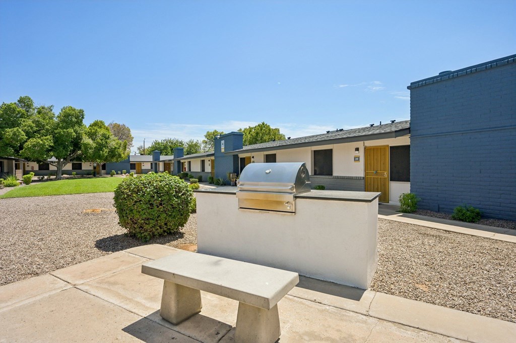 A bench is in the foreground of a sunny courtyard with a building in the background.