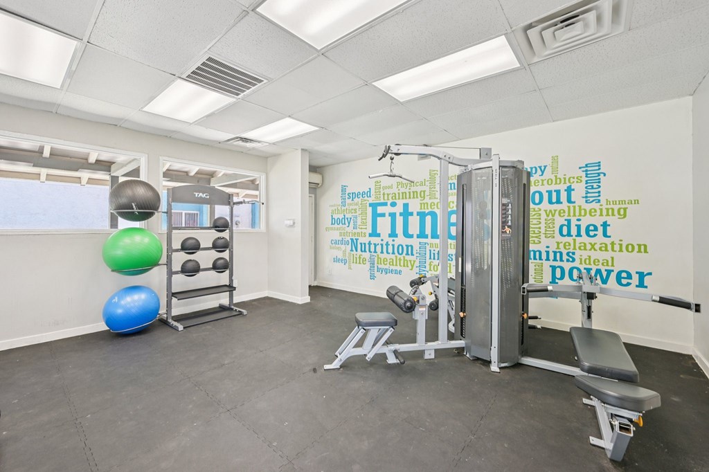 A gym room with a weight machine, a bench, and a ball.