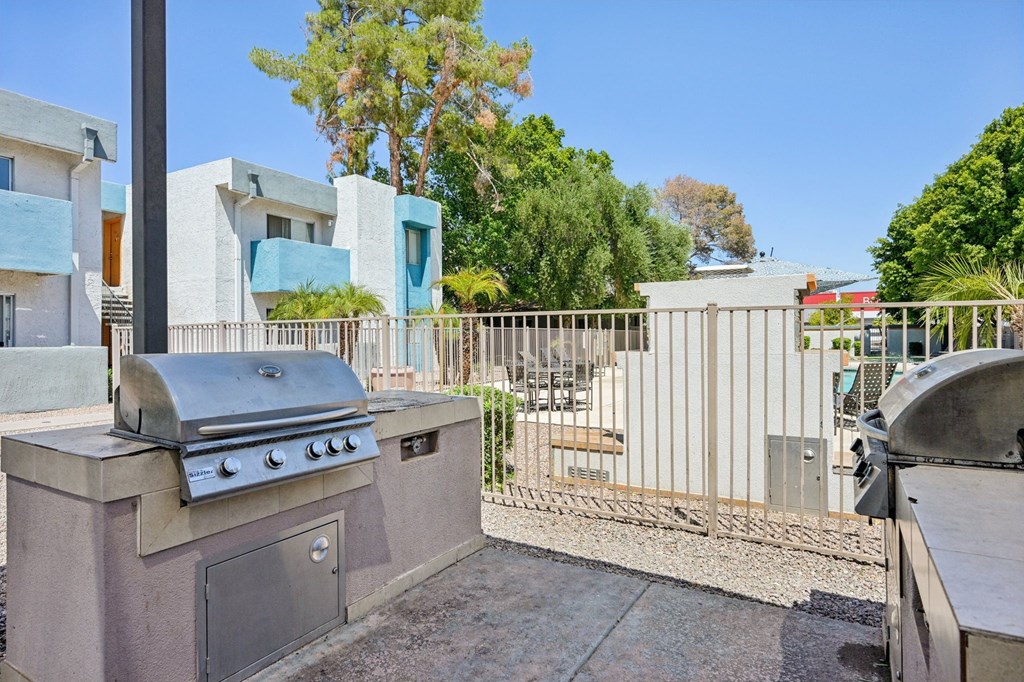 A barbecue grill is in the foreground of a sunny backyard.