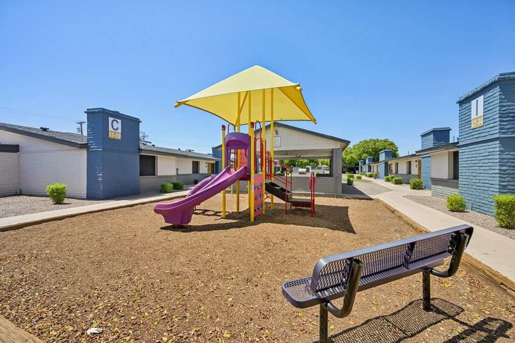 A playground with a yellow umbrella and a purple slide.