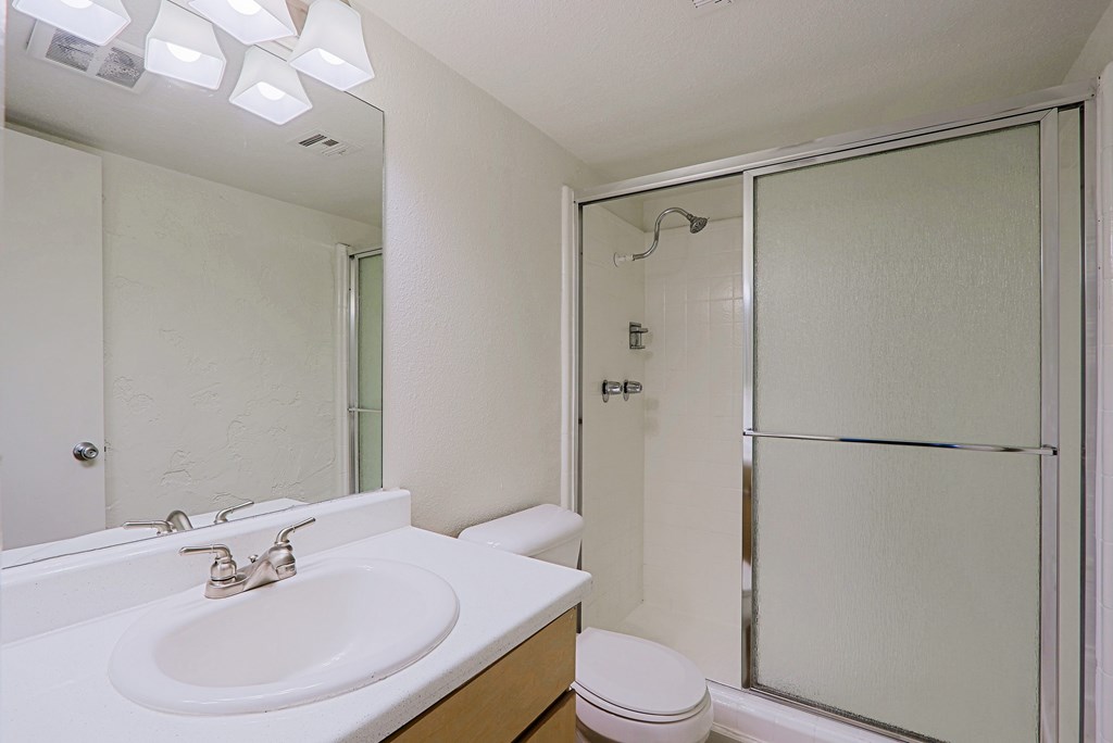 A white bathroom with a sink, toilet, and shower.