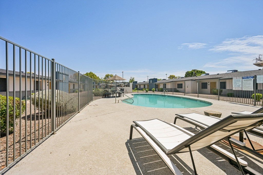 A pool area with sun loungers and a fence.