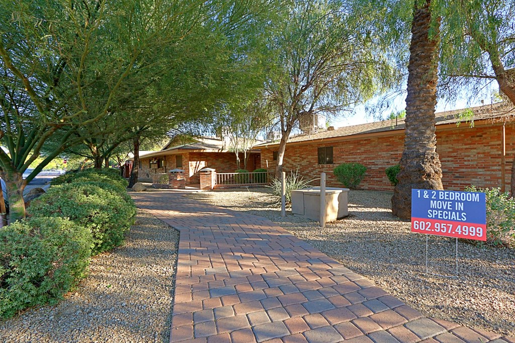 a pathway leading to a brick house with trees and a sign
