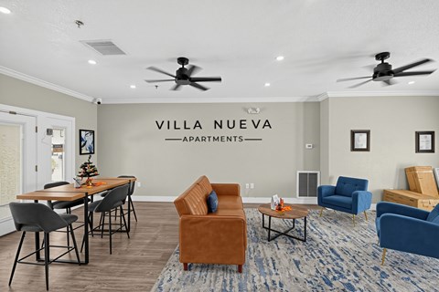A living room with a sofa, chairs, and a dining table with a sign that says "VILLA NUEVA APARTMENTS".