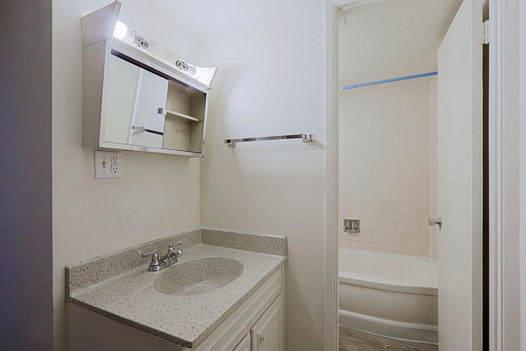 A bathroom with a sink, mirror, and bathtub.
