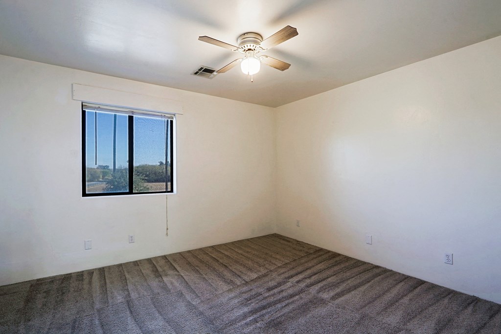 A room with a ceiling fan and a window overlooking a field.