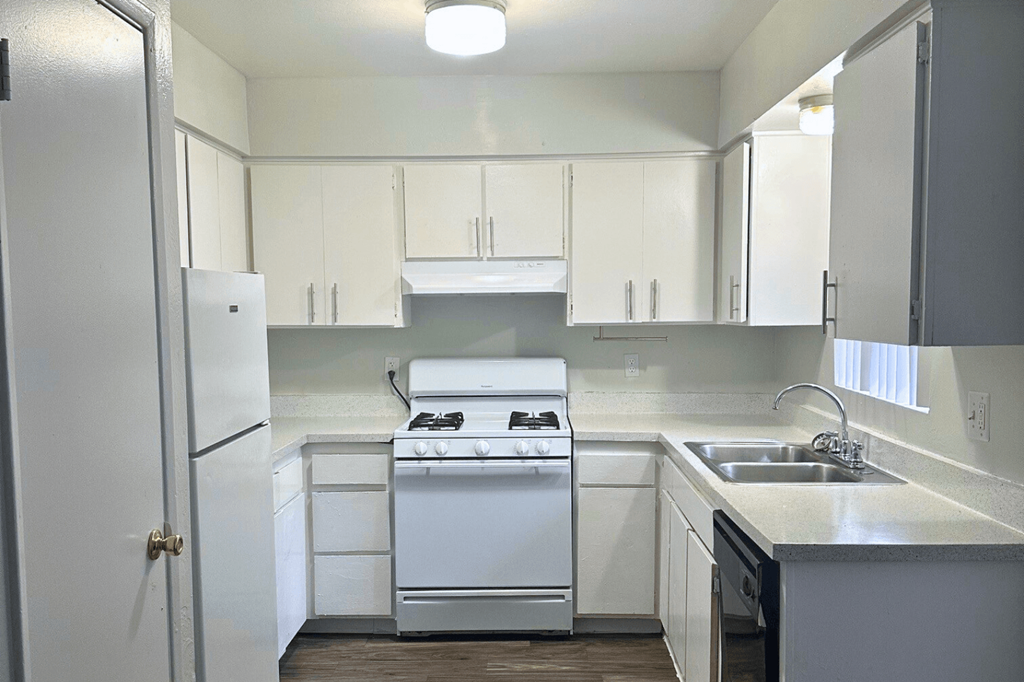 A white kitchen with a stove, sink, and cabinets.