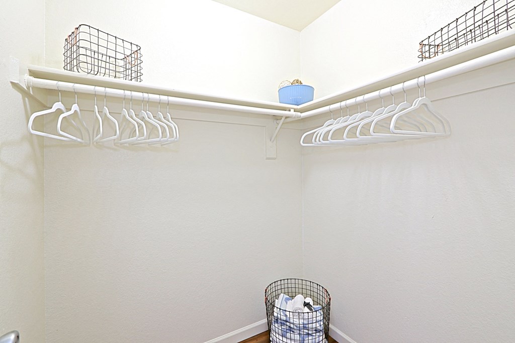 a walk in closet in a bathroom with white walls and a white rack with white hangers