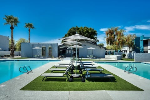 a pool with lounge chairs and umbrellas next to a building at Connect on Missour Apartments, Arizona