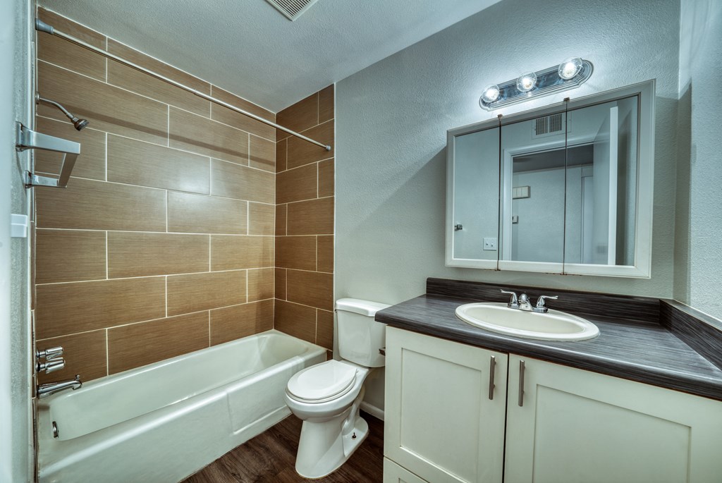 A bathroom with a white toilet, a white sink, and a brown tiled wall. at Connect on University, Mesa, 85203