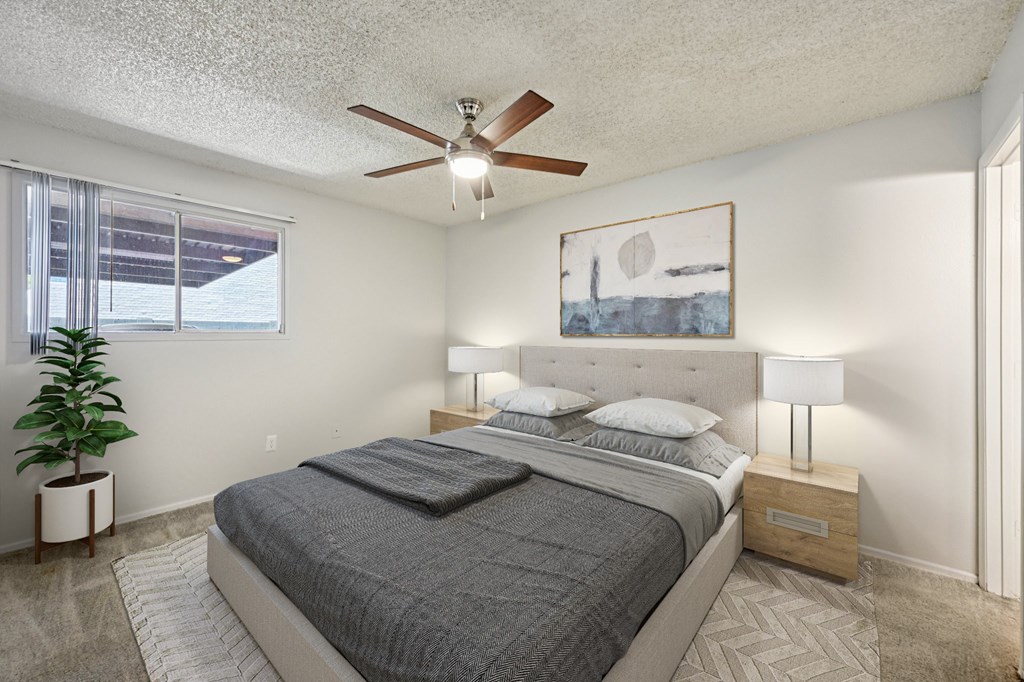 A bedroom with a large bed, a ceiling fan, and a painting on the wall.