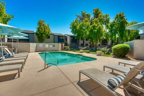 a swimming pool with lounge chairs and umbrellas and buildings in the background at Connect on Northern, Glendale, AZ