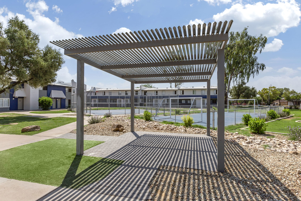 a pergola in front of a building with a tennis court