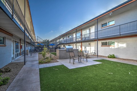 a patio with a grill and chairs in front of a building