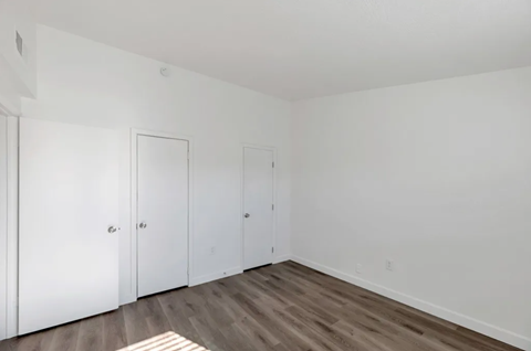 a bedroom with white walls and wooden floors and two closets