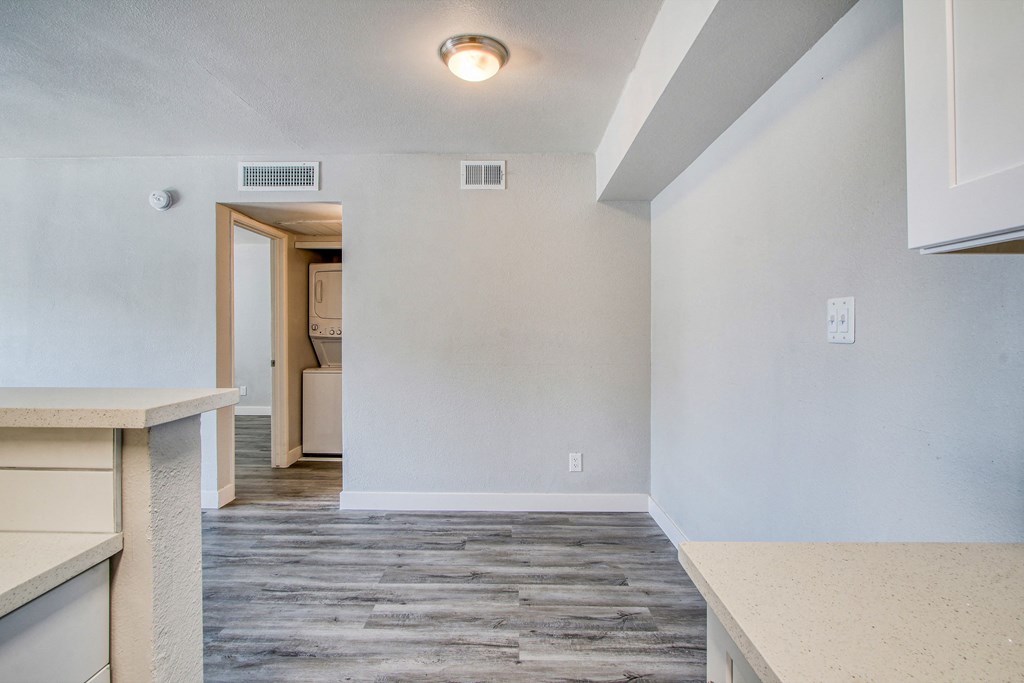the living room and kitchen of an apartment with white walls and wood flooring