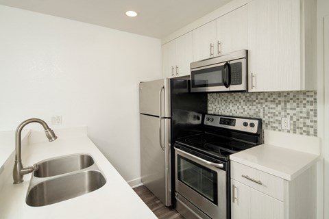 A kitchen with a stainless steel sink and black appliances.