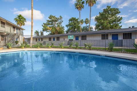 A swimming pool in front of a building with palm trees.