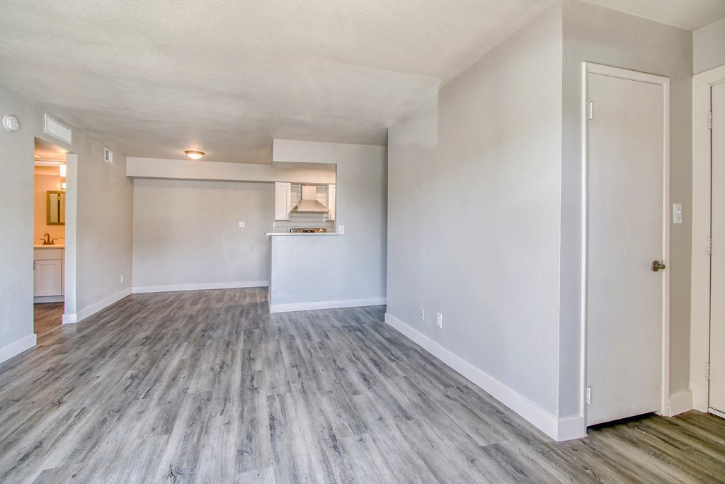 the living room and kitchen of an apartment with white walls and wood flooring