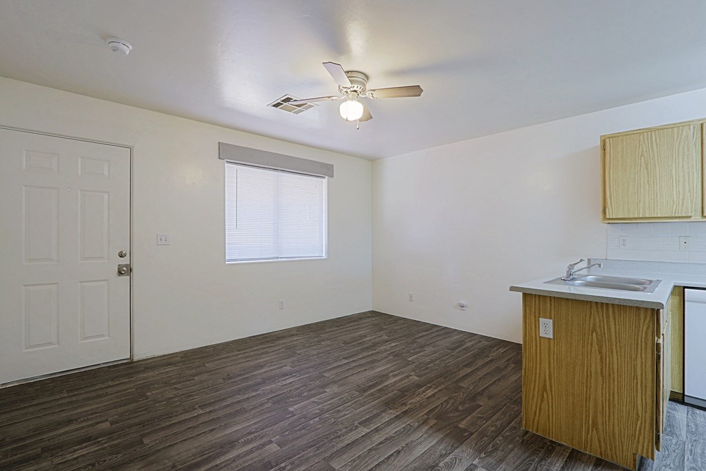 A room with a white ceiling, a window with blinds, a wooden floor, a white sink, and a wooden cabinet.