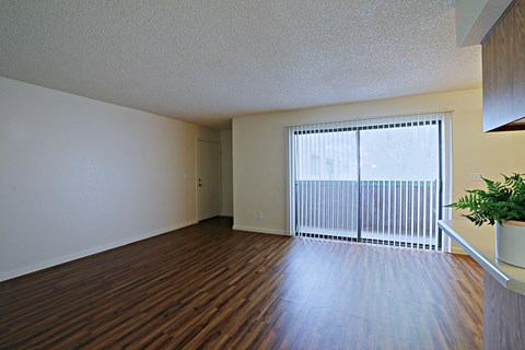 the spacious living room of an apartment with a large window and wood flooring