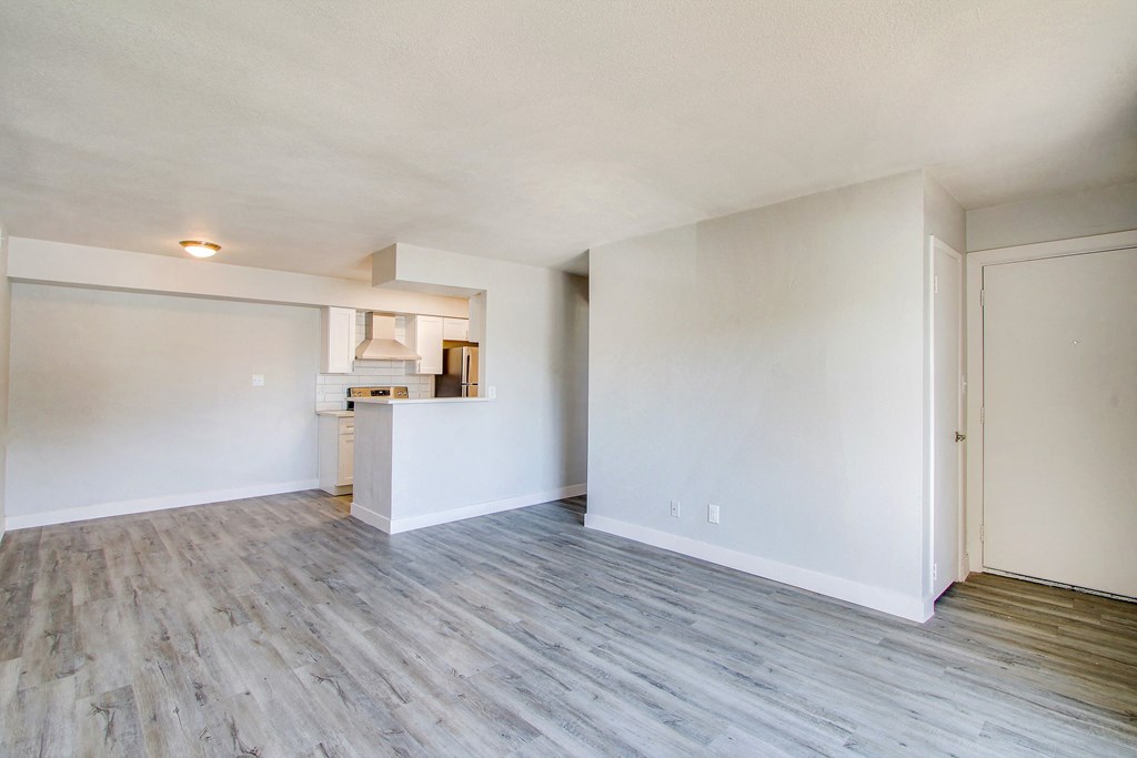 the living room and kitchen of an apartment with white walls and wood flooring
