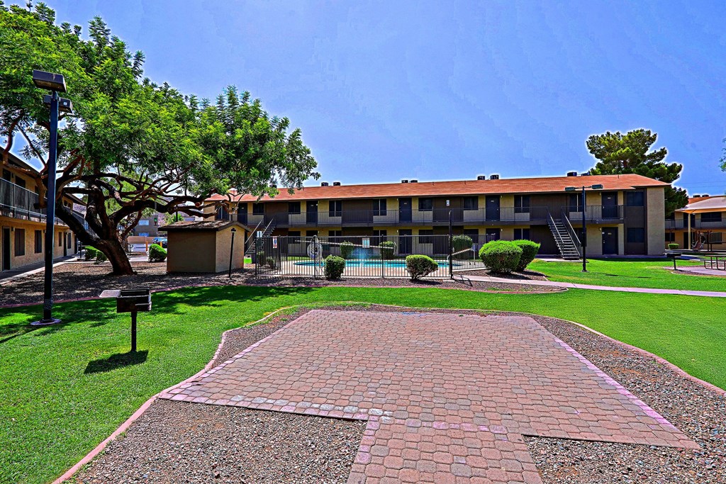 A brick walkway leads to a building with a pool in the front yard.