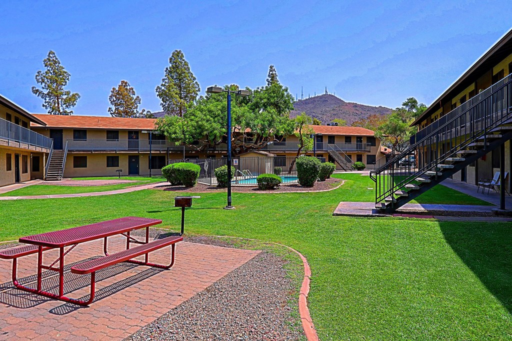 A red picnic table is in the middle of a grassy courtyard.