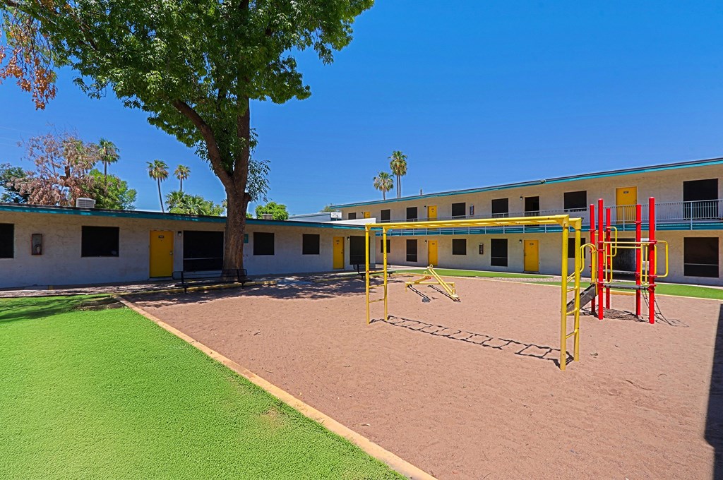 A playground with a red and yellow swing set in front of a building with yellow doors.