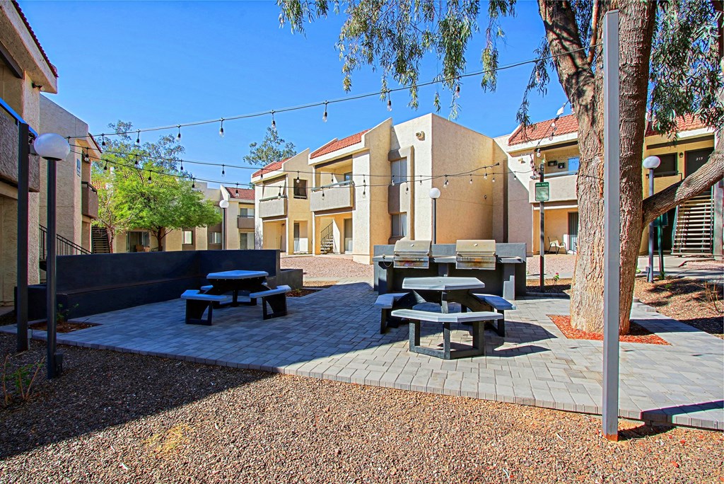 a courtyard with picnic tables and benches and buildings in the background