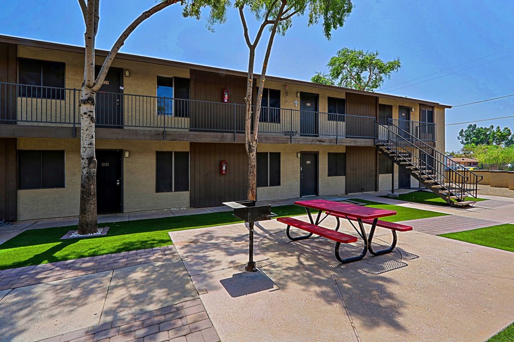 A red picnic table is in front of a building with balconies.