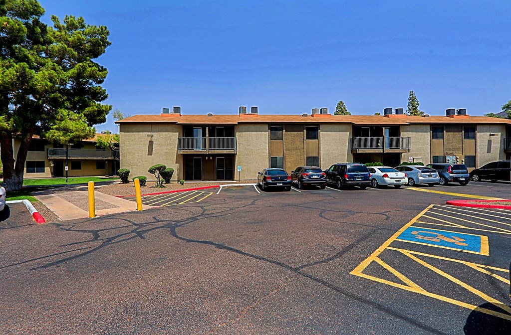 A parking lot with a building in the background and a few cars parked.