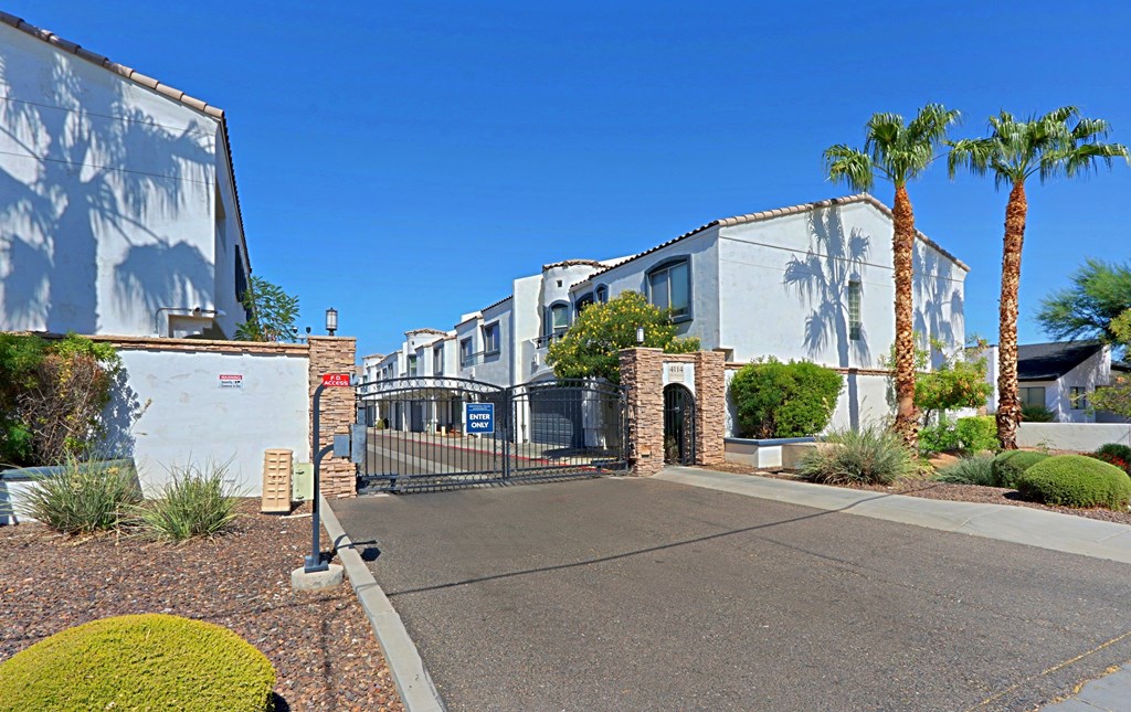 A sunny day at a gated community with palm trees and white houses.