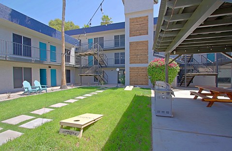 A patio with a table and chairs is surrounded by a grassy area and a building.