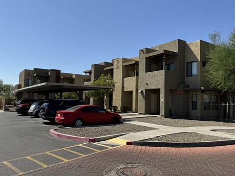 A red car is parked in a parking lot in front of a building.