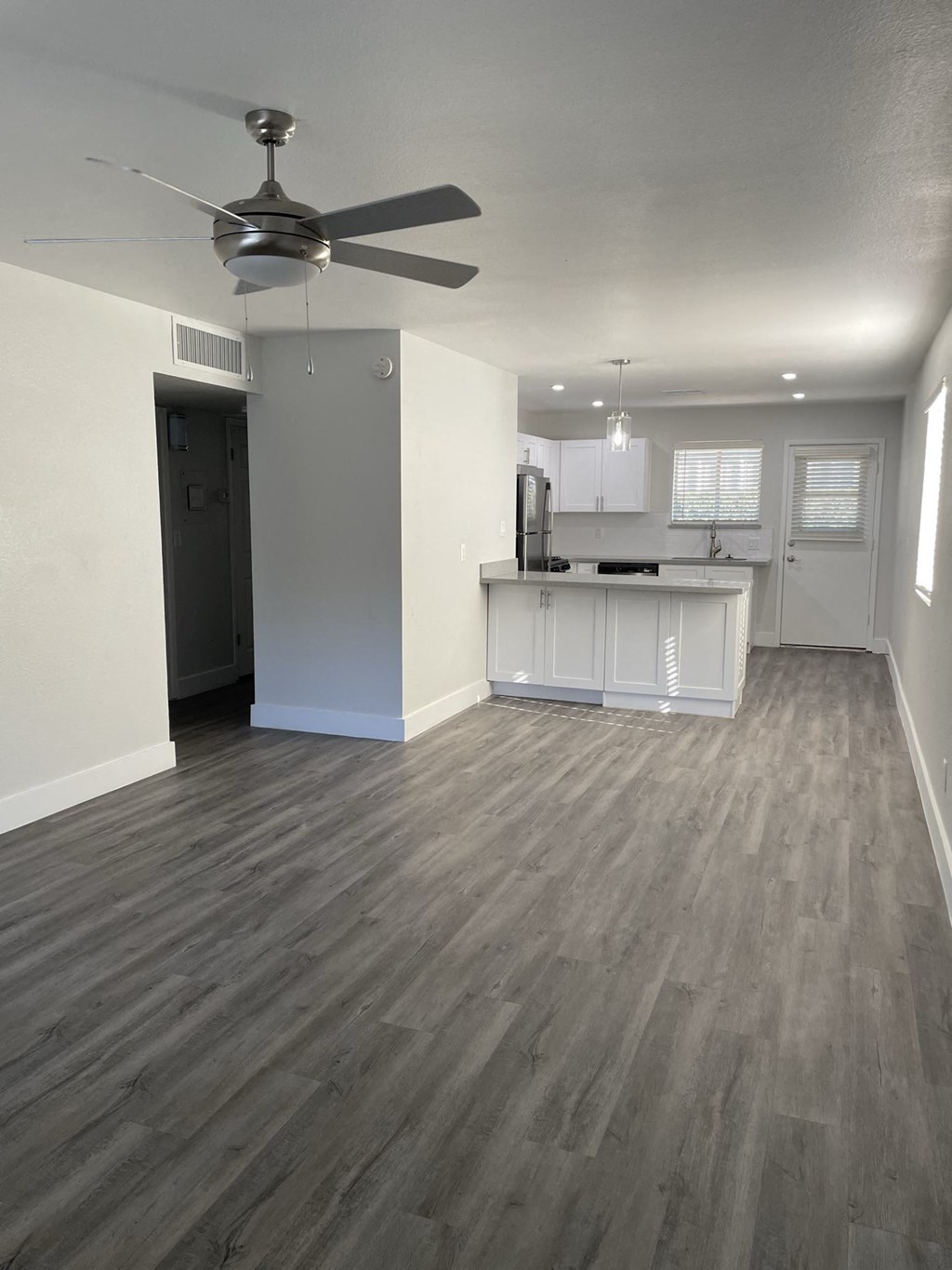 an empty living room with a kitchen and a ceiling fan