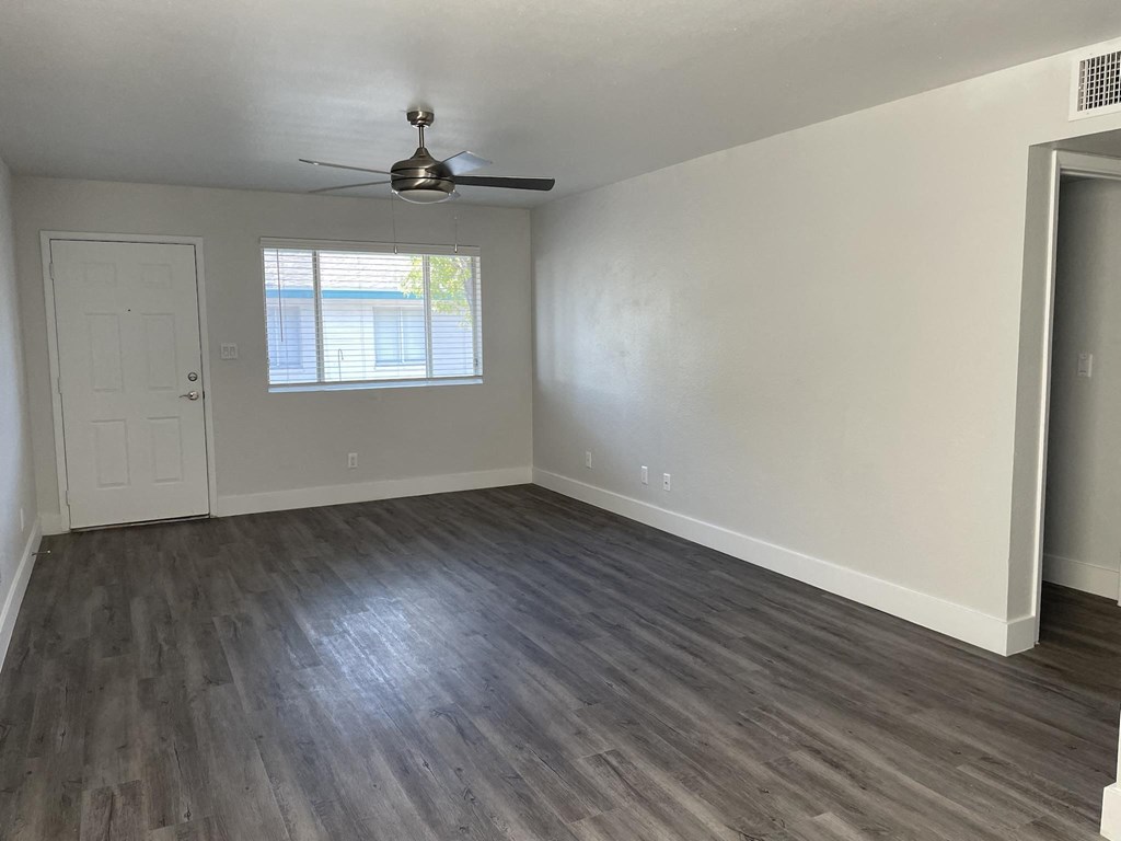 an empty living room with wooden floors and a ceiling fan