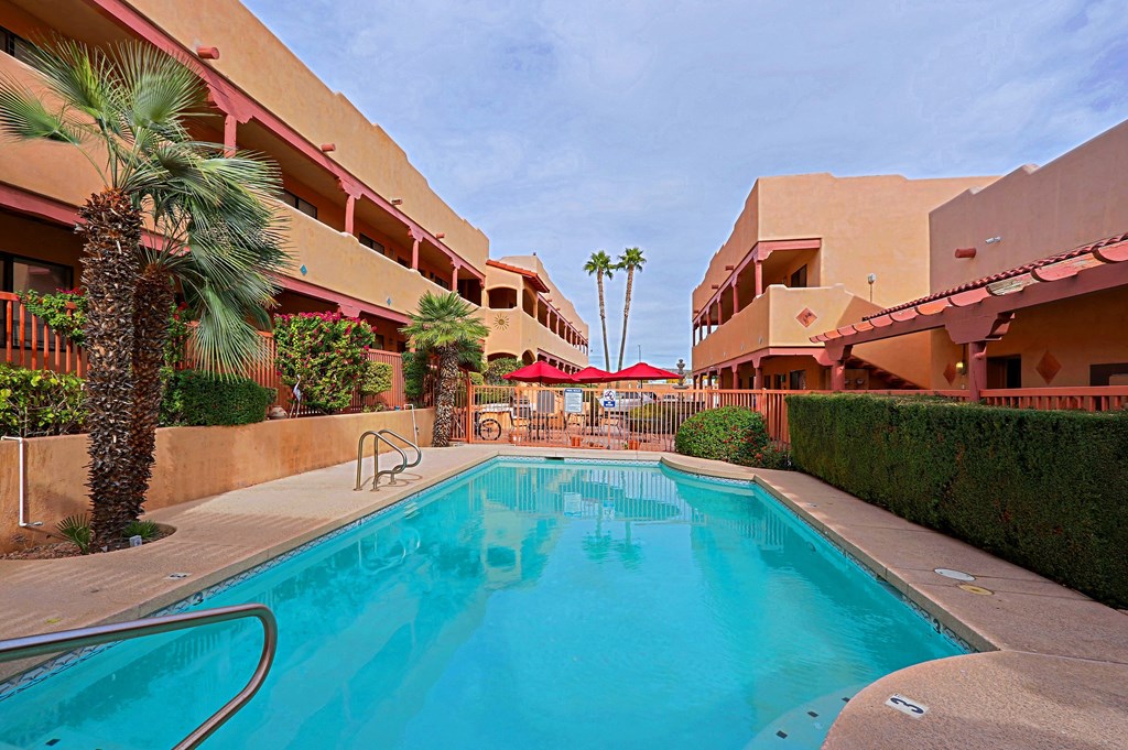 A swimming pool is surrounded by a building and palm trees.