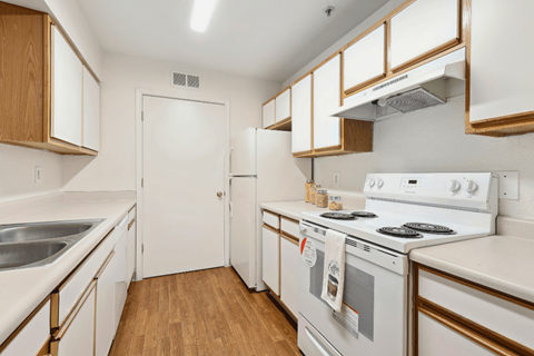 a kitchen with white appliances and wood flooring and white cabinets