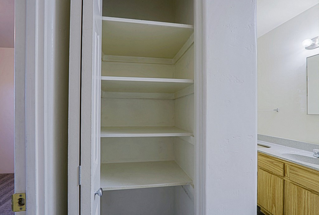A white open closet with shelves and a mirror in the background.