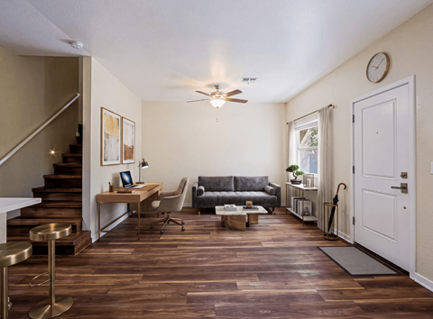 A living room with a gray couch, a table and chair, a coffee table, and a staircase leading to the second story.